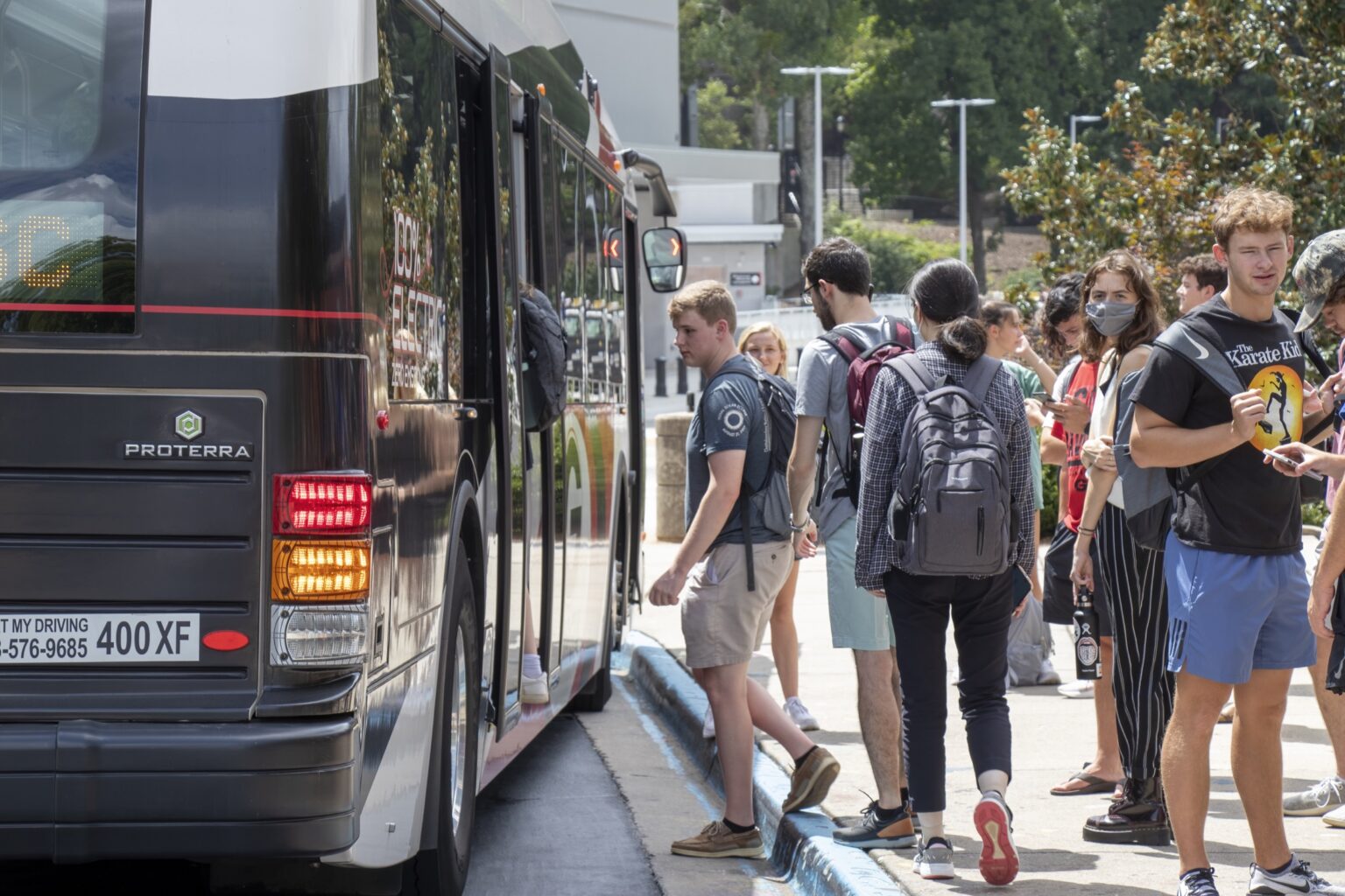 Students, some wearing face masks, board a bus at a university campus.