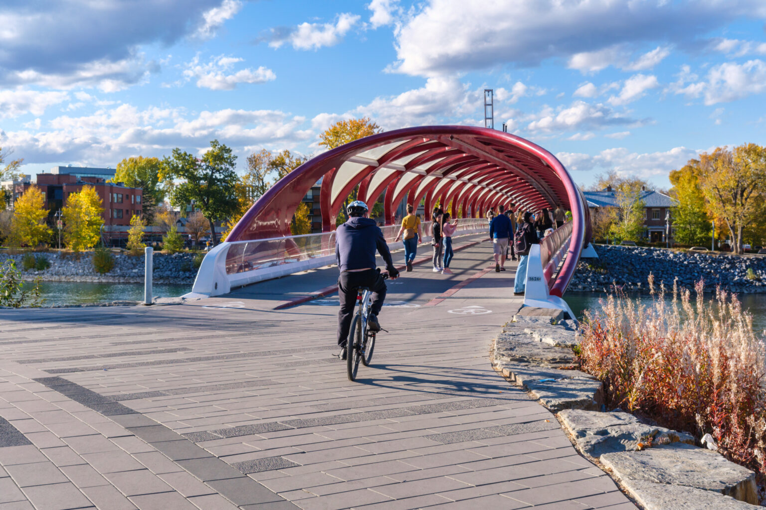 Person on bicycle rides onto bridge with vibrant red roof in Calgary, Alberta, Canada