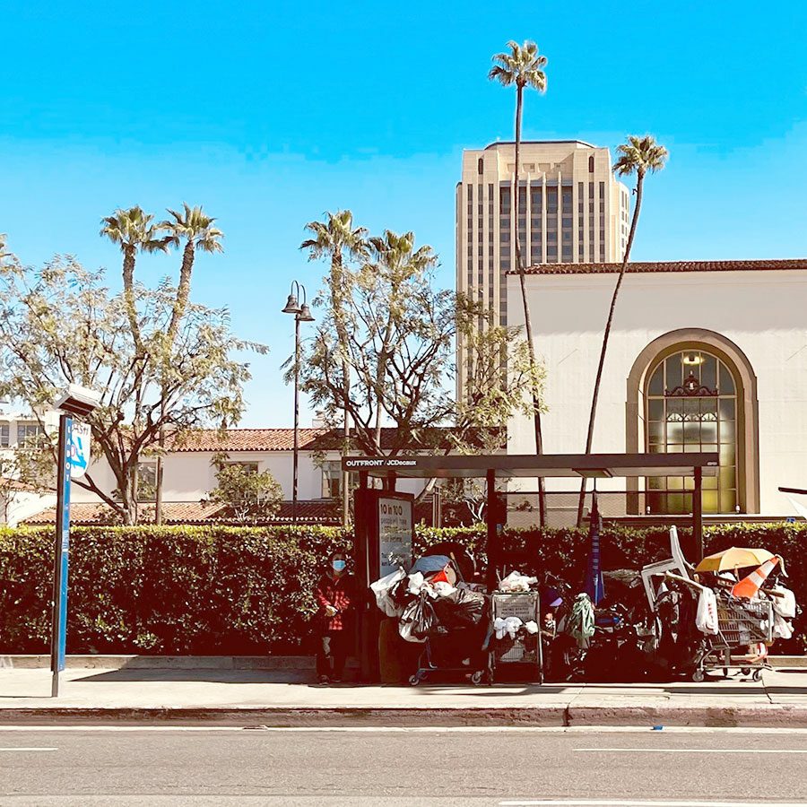 Person waits for the bus next to a transit shelter in LA being used as shelter by a homeless person. Credit LA Metro, Stephanie Wiggins