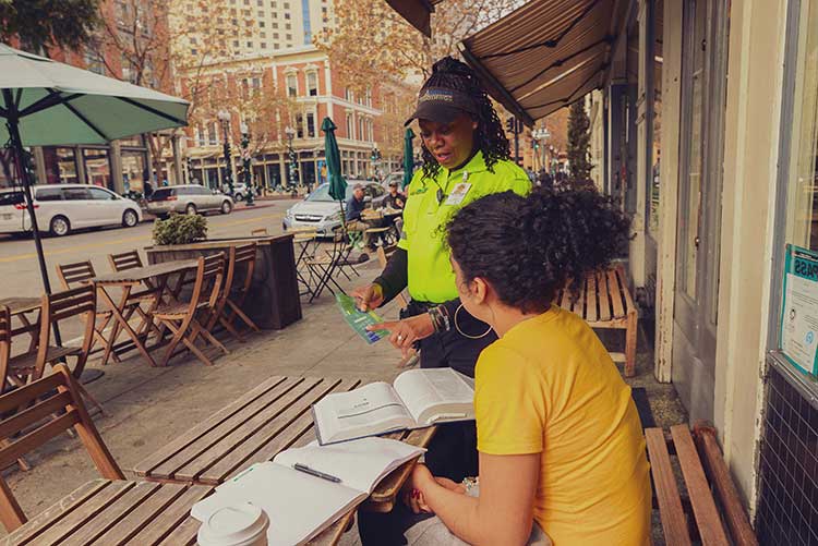A downtown Ambassador talks to a woman working at an outdoor table in Oakland CA. Courtesy Downtown/Uptown CBDs Oakland CA