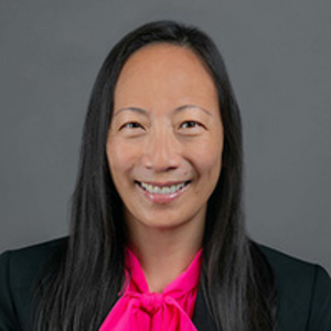 Nadine Lee in a suit smiling in front of a gray background.