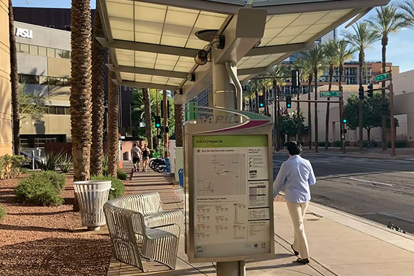 Person walking by transit stop in Phoenix, scooters and buildings in background