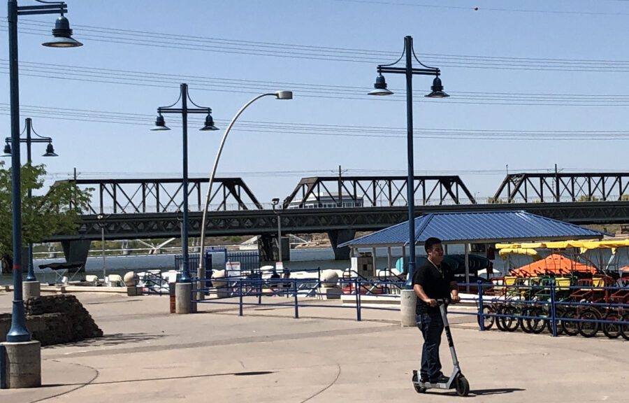 Person scootering on a wide sidewalk next to Tempe Town Lake